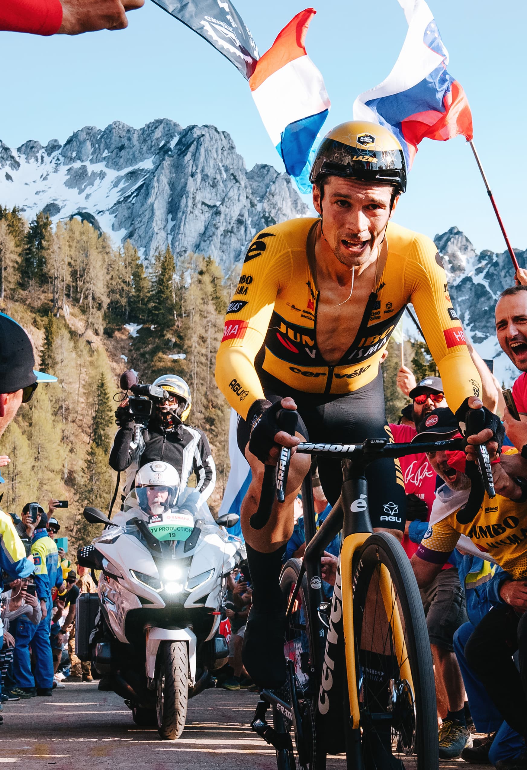 Primož Roglič races past a crowd of loud, cheering fans waving flags and signs. He is riding a Cervélo R5 and approaching the finish of the Stage 20 time trial of the Giro d’Italia.