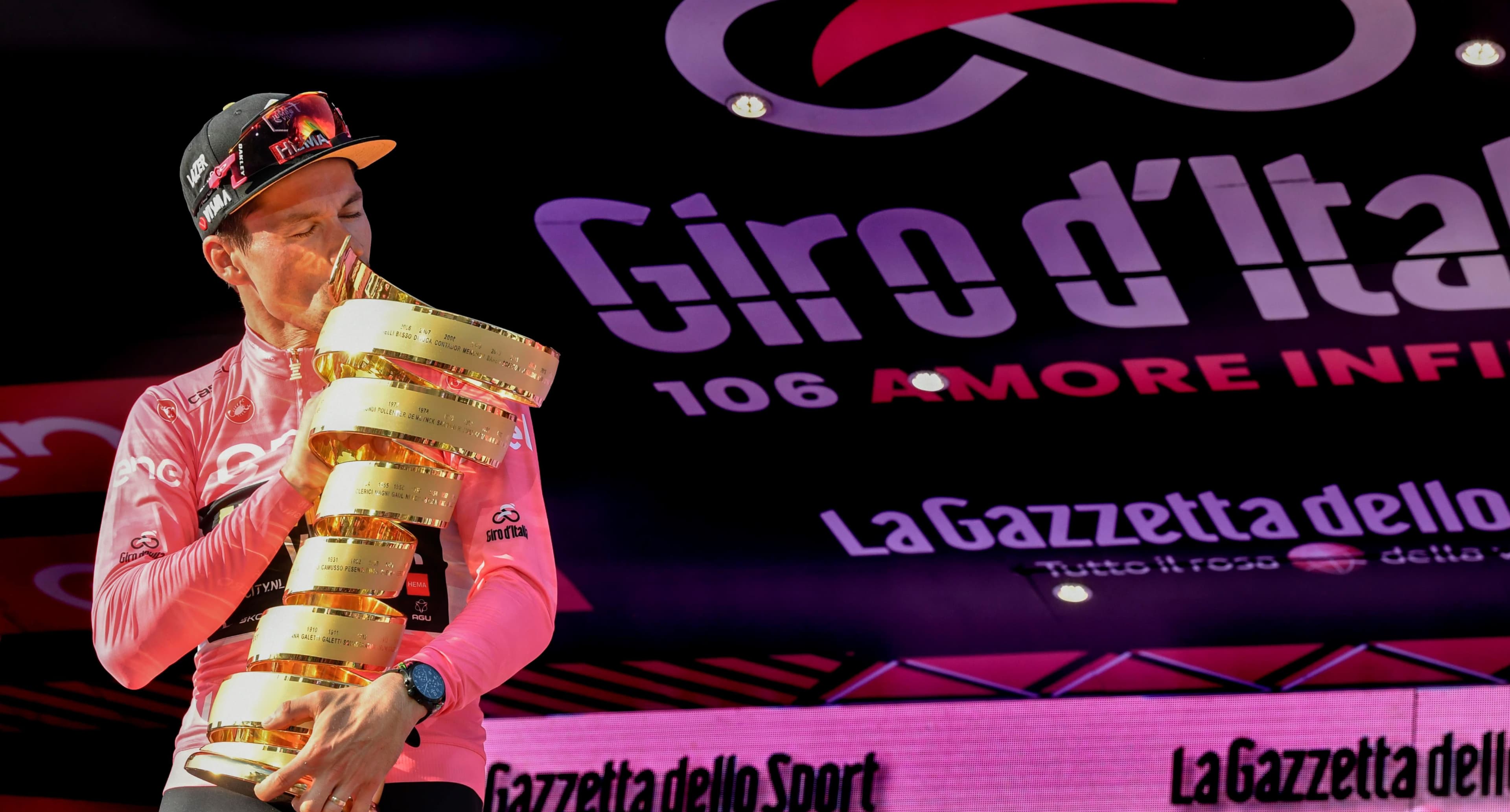 Primož Roglič wearing the Pink jersey stands on the top step of the Giro d’Italia podium and kisses the winner’s trophy.