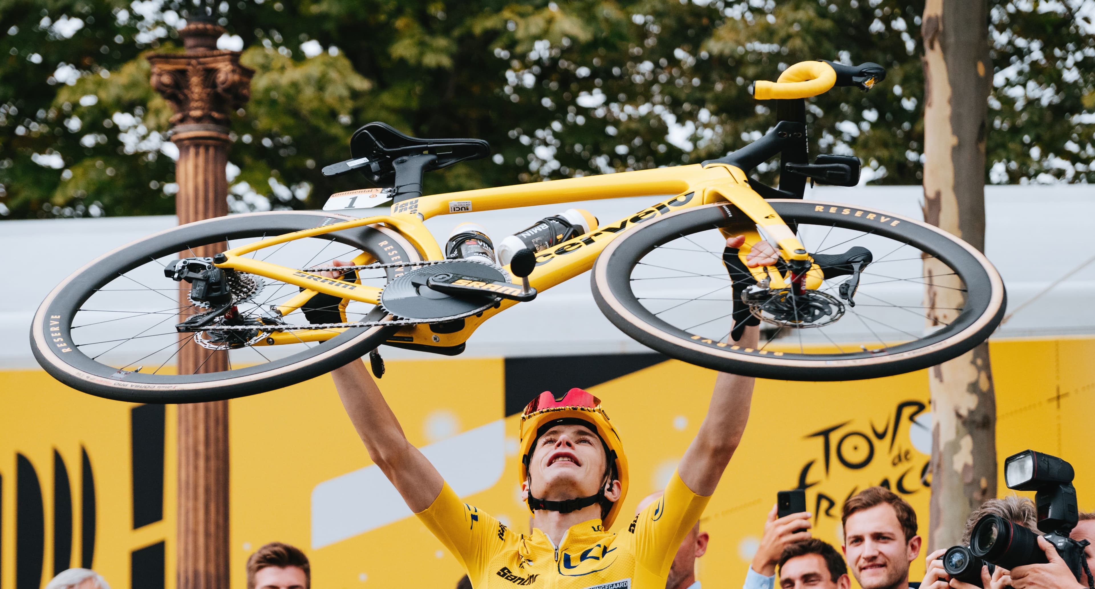 Jonas Vingegaard lifts his special-edition yellow Cervélo S5 above his head in a celebration of victory.