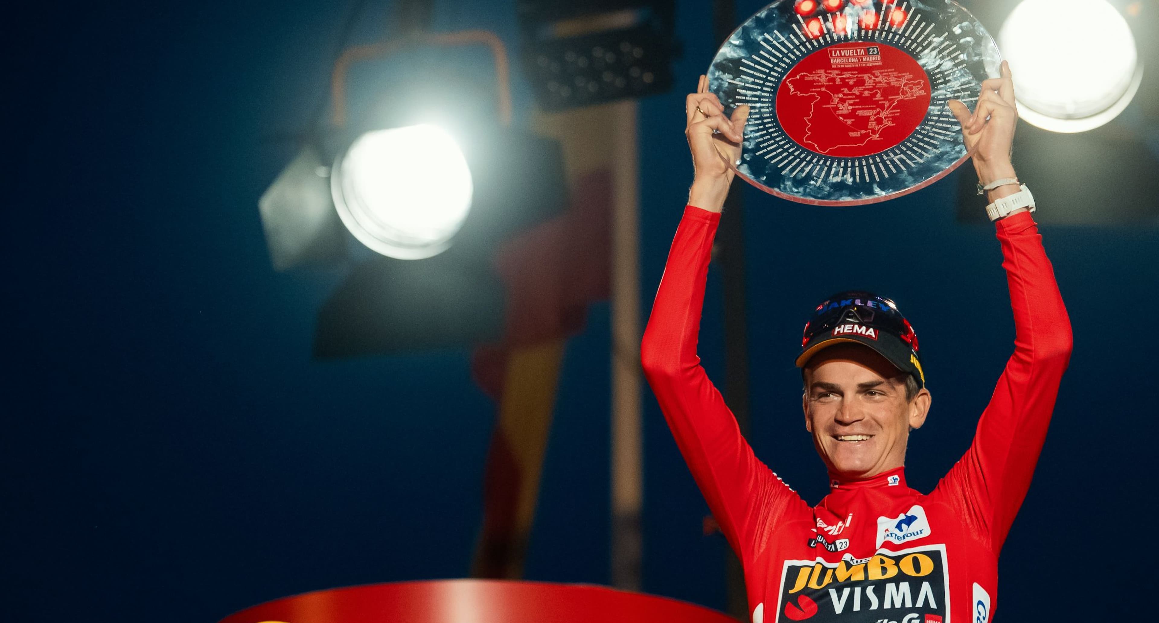 Sepp Kuss in the Red Jersey holding the glass trophy of the Vuelta a España above his head in celebration.