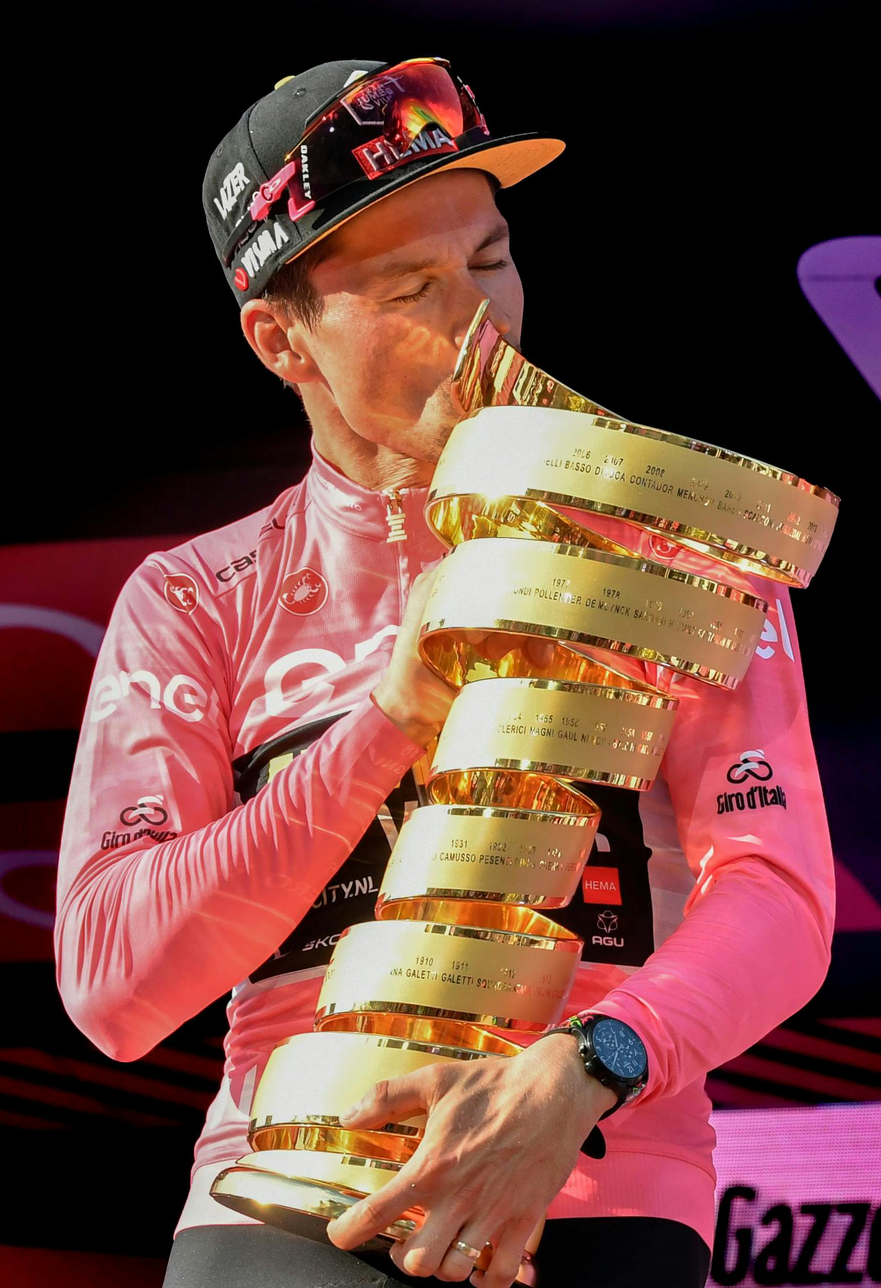 Primož Roglič wearing the Pink jersey stands on the top step of the Giro d’Italia podium and kisses the winner’s trophy.