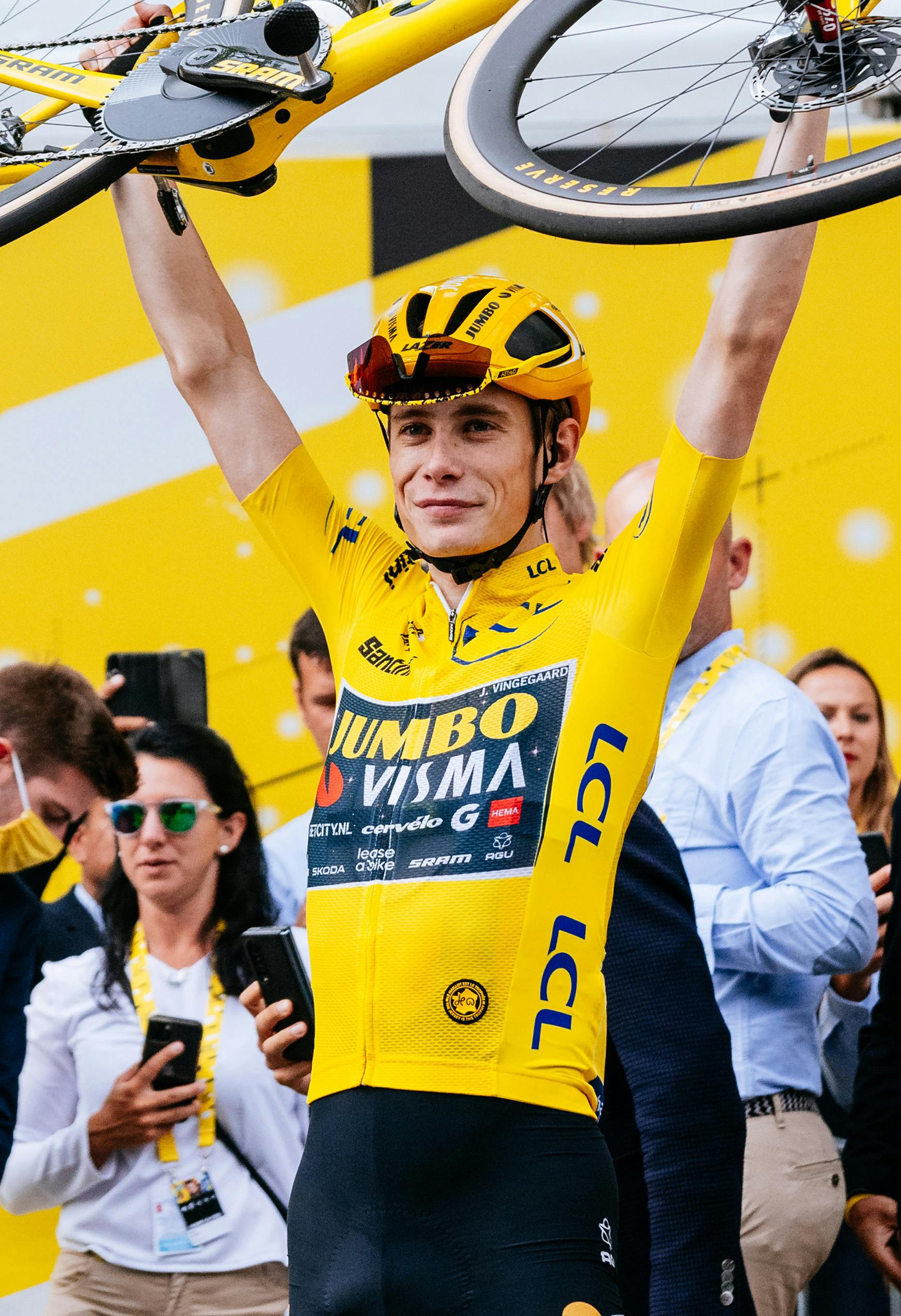 Jonas Vingegaard lifts his special-edition yellow Cervélo S5 above his head in a celebration of victory.