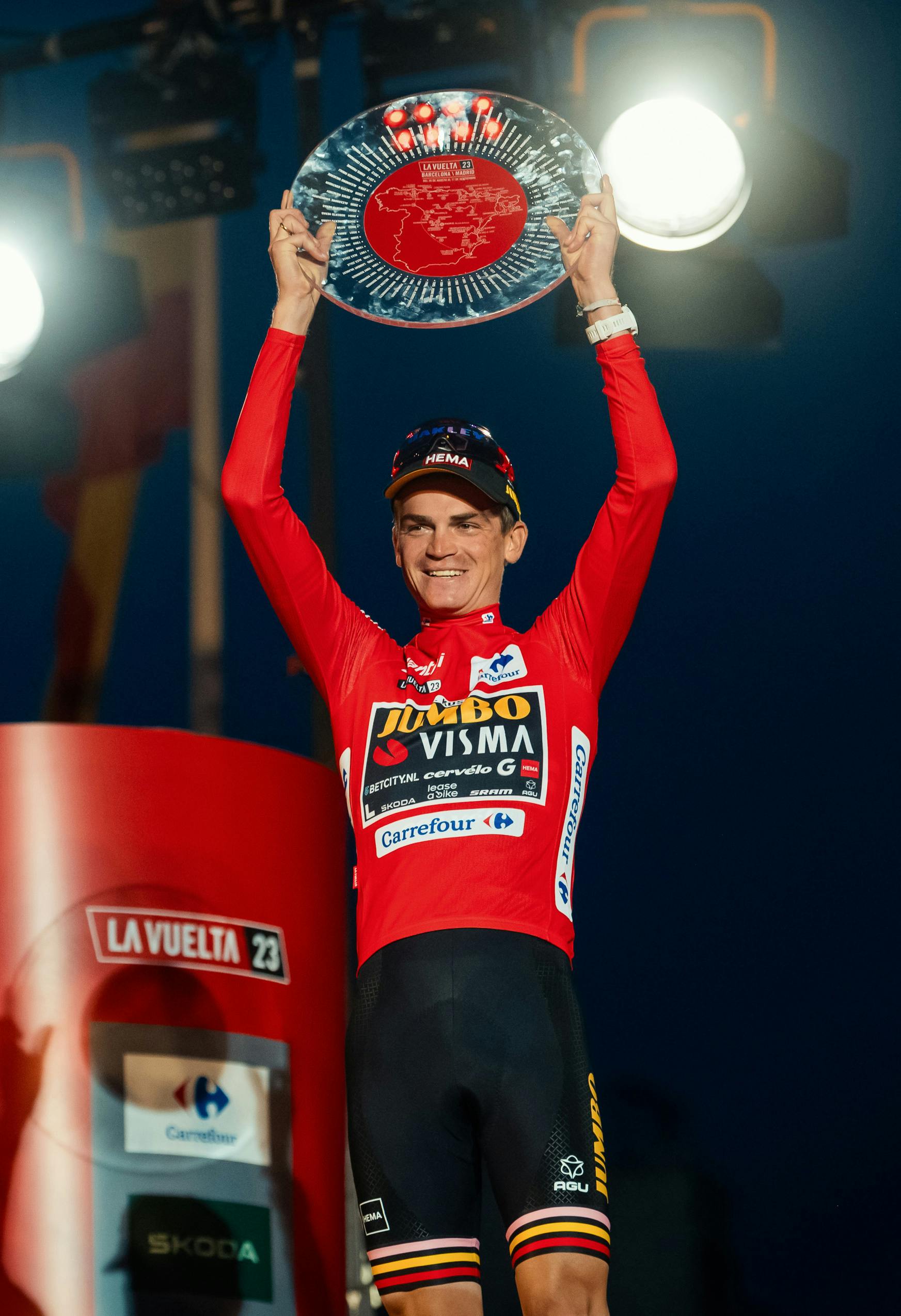 Sepp Kuss in the Red Jersey holding the glass trophy of the Vuelta a España above his head in celebration.