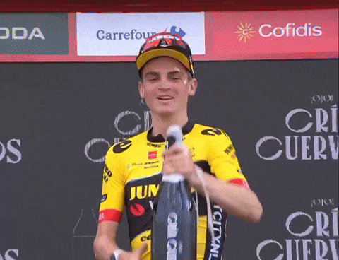 Sepp Kuss chugging champagne from the bottle while standing on the podium
